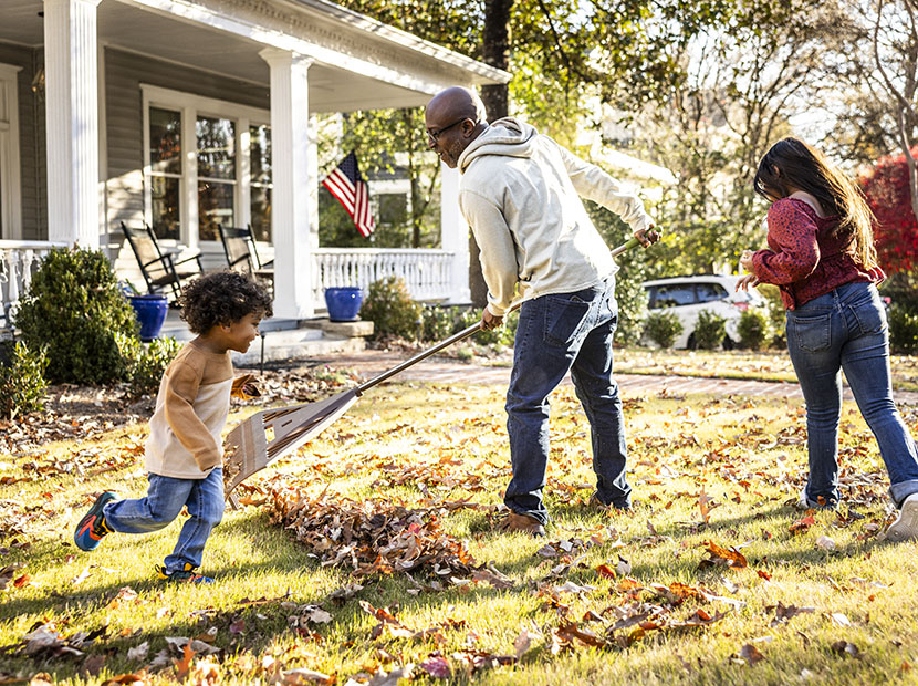 Parent raking leaves in front yard while children play